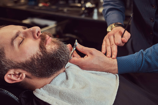 Cabeleireiro profissional modelando barba com tesoura e pente na barbearia. Foto de close-up
. - Foto, Imagem