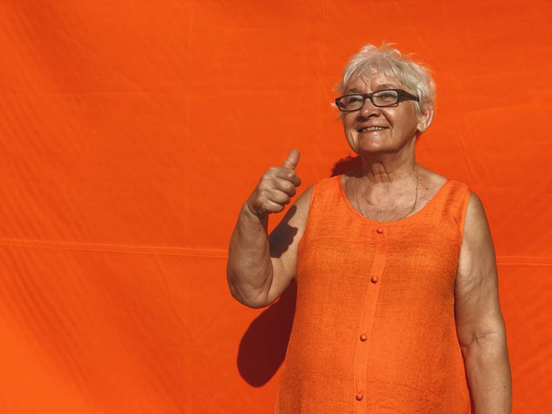 Eristetty luonnollinen laukaus ilman korjausta vanhempi nainen poseeraa oranssi tyhjä seinä tausta mainostilaa. Näytän tunteita kameralle. Nainen, jolla on hamstrauspää ja joka ilmaisee tunteita.
. - Valokuva, kuva