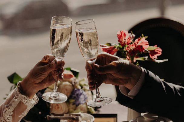 Cheers! Unrecognizable woman and man clink glasses of wine or champagne, celebrate something, dressed in formal festive clothes. Bride and groom with beverage - Фото, изображение