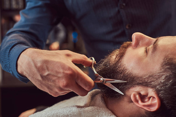Professional hairdresser modeling beard with scissors and comb at the barbershop. Close-up photo. - Photo, Image