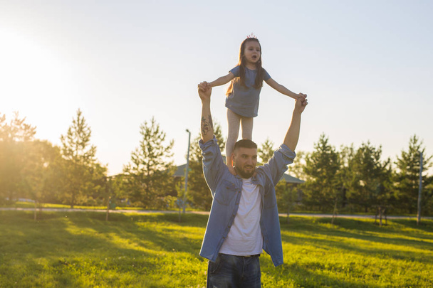 Happy man holding his little daughter on neck in summer park - Fotoğraf, Görsel