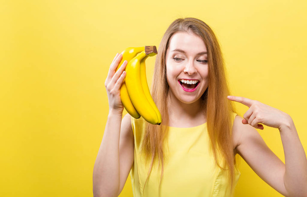 Happy young woman with bananas on a yellow background - Valokuva, kuva