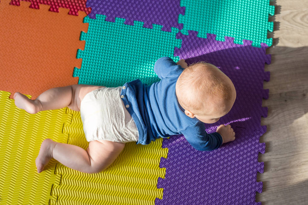 Infant baby boy playing on colorful soft mat. Little child  making first crawling steps on floor. Top view from above - Photo, Image