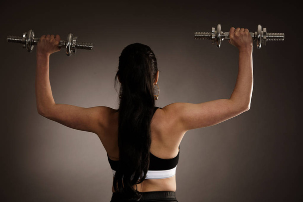 Woman work out arms with dumbbells over gray background - 写真・画像