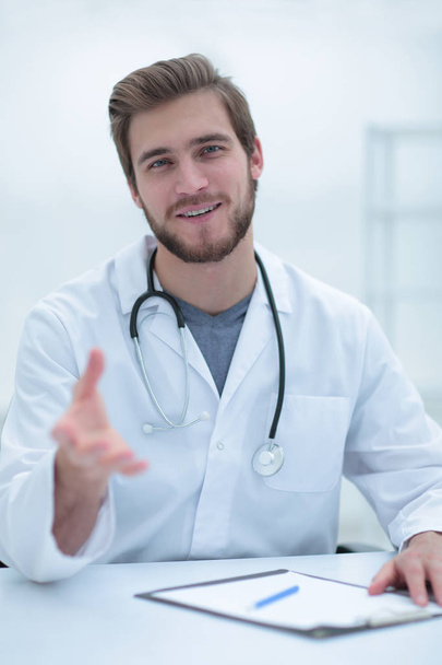 Handsome medical doctor in white coat is offering his hand - 写真・画像