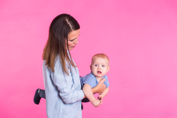 family, motherhood, parenting, people and child care concept - happy mother holds adorable baby over pink background - Foto, Imagem