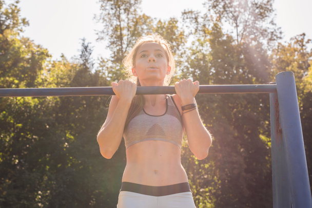 young athletic fitness woman working out at outdoor gym doing pull ups at sunrise. - Fotoğraf, Görsel