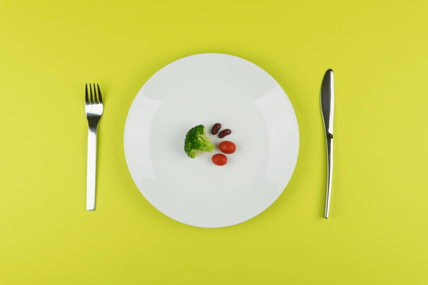 Диетическая концепция, небольшое количество салата на белой круглой тарелке с вилкой и ножом
 - Фото, изображение
