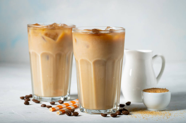 背の高いグラスに注がれるクリームとコーヒー豆のアイス コーヒー。明るい青の背景に冷たい夏の飲み物 - 写真・画像