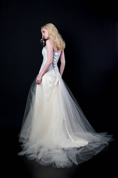 full length portrait of model wearing white bridal ball gown, standing pose on black background. - Foto, Bild