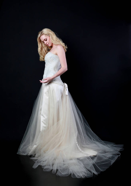 full length portrait of model wearing white bridal ball gown, standing pose on black background. - Foto, Imagen