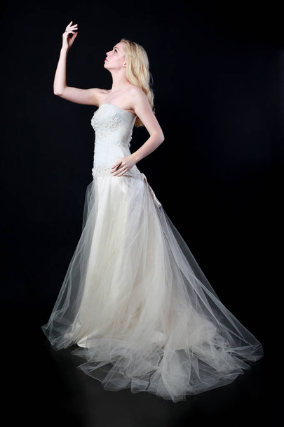 full length portrait of model wearing white bridal ball gown, standing pose on black background. - Fotó, kép