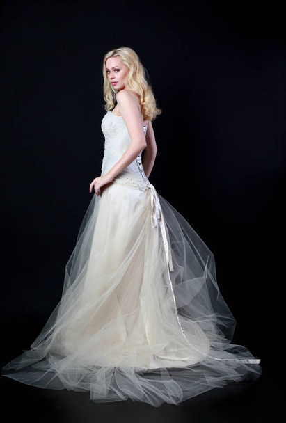 retrato de longitud completa de modelo con vestido de novia blanco, pose de pie sobre fondo negro
. - Foto, Imagen
