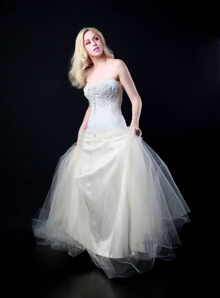 retrato de longitud completa de modelo con vestido de novia blanco, pose de pie sobre fondo negro
. - Foto, Imagen