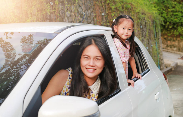 Ευτυχισμένος νεαρή γυναίκα και παιδί κοριτσάκι κάθεται σε ένα αυτοκίνητο και να αναζητούν την φωτογραφική μηχανή από τα windows. Οικογενειακά ταξίδια έννοια. - Φωτογραφία, εικόνα