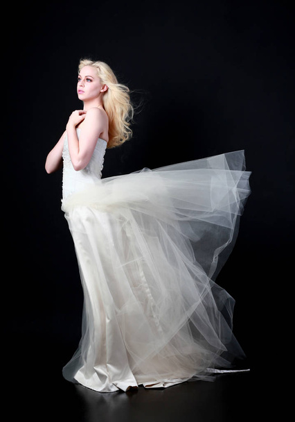retrato de comprimento total do modelo vestindo vestido de baile de noiva branco, em pé posar sobre fundo preto
. - Foto, Imagem
