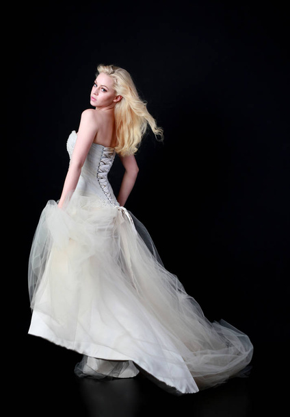 full length portrait of model wearing white bridal ball gown, standing pose on black background. - Foto, afbeelding
