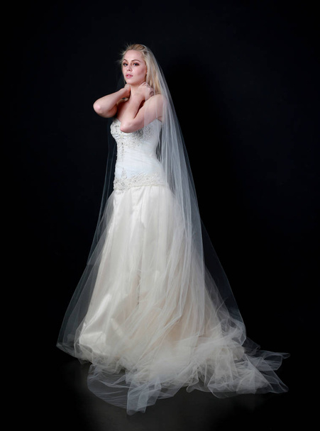 retrato de comprimento total do modelo vestindo vestido de baile de noiva branco, em pé posar sobre fundo preto
. - Foto, Imagem