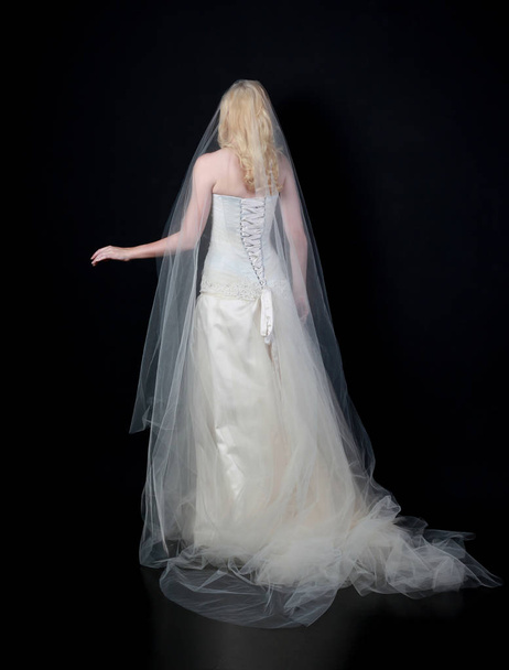 volledige lengte portret van model draagt witte bruids bal toga, staande pose op zwarte achtergrond. - Foto, afbeelding