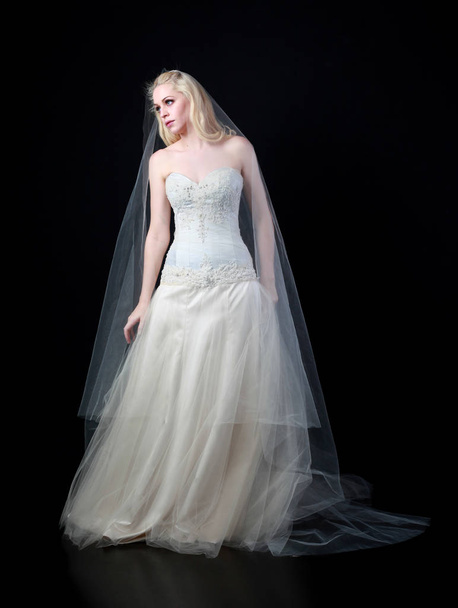 full length portrait of model wearing white bridal ball gown, standing pose on black background. - Foto, Bild