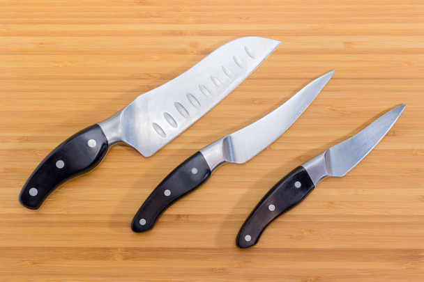 Tres cuchillos de cocina diferentes en la tabla de cortar de bambú
 - Foto, imagen