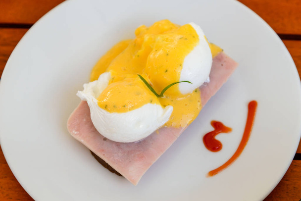 Benedicto de huevo en el plato blanco en el desayuno - Huevo escalfado en rodajas de jamón y un pedazo de pan
 - Foto, Imagen