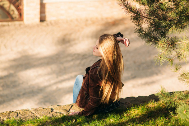 A beautiful girl is walking along the embankment. Blond hair and brown jacket. Spring - Φωτογραφία, εικόνα