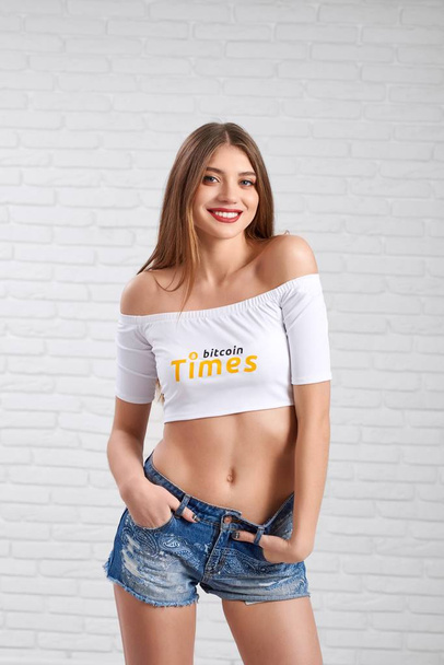 Smiling sporty beautiful female model in denim shorts and white crop top with bitcoin logo - Foto, afbeelding