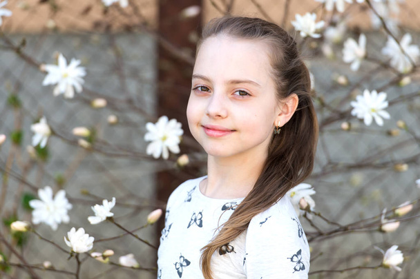 Child with blossoming flowers outdoor. Little girl on floral blossom in spring. Beauty kid with fresh look and long hair. Spring, easter and holidays celebration concept - Foto, Imagem