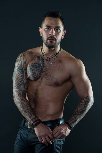 Bearded man with tattooed body. Macho with sexy bare torso in jeans. Tattoo model with six pack and ab. Athlete or sportsman with muscular chest and belly. Sport or fitness and bodycare - 写真・画像