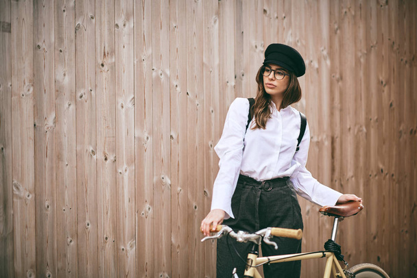 Portrait of beautiful brunette holding bicycle. Wooden background. - 写真・画像
