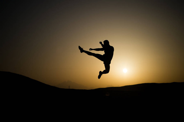 Спортсмен стрибає високо з енергією. Спортивний силует на небі заходу сонця. Навчання людини на природному ландшафті. Тренування в літній сутінці. Спорт, оздоровлення та концепція догляду за тілом
 - Фото, зображення