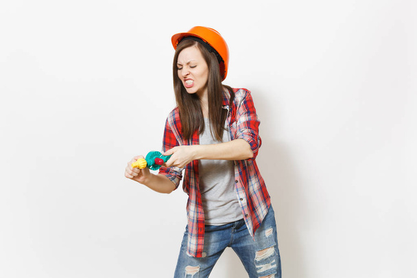 Irritierte verrückte Frau in lässiger Kleidung und orangefarbenem Bauhelm mit Spielzeugbohrer auf weißem Hintergrund. Instrumente, Werkzeuge für die Renovierung der Wohnung Zimmer. Heimkonzept reparieren. - Foto, Bild