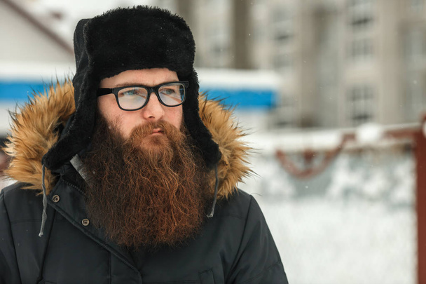 Bearded man in real life. Portrait of young guy with large beard in glasses and a black cap in the winter. - Foto, immagini