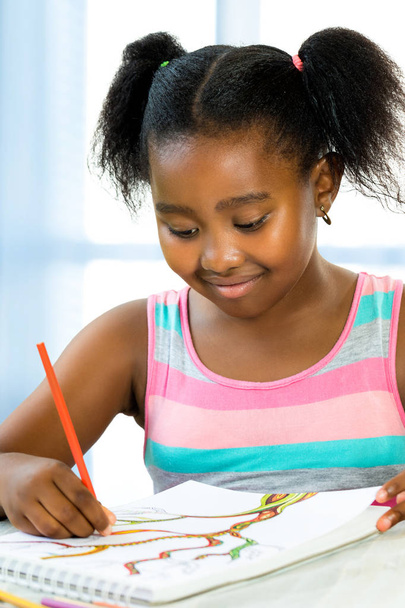 Ritratto ravvicinato della piccola ragazza africana creativa che disegna alla scrivania.Bambino che crea un disegno colorato con matite a colori
. - Foto, immagini