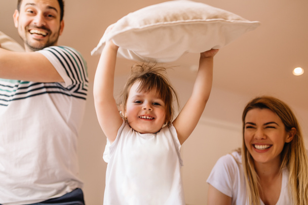 Cute little girl is playing with pillows with her parents - Foto, immagini