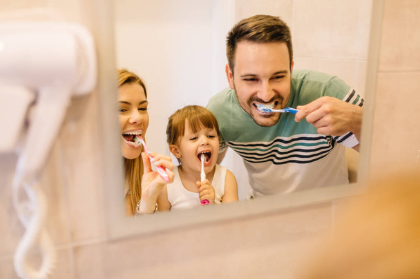 Onnellinen perhe harjaa hampaitaan peilin edessä kylpyhuoneessa
 - Valokuva, kuva