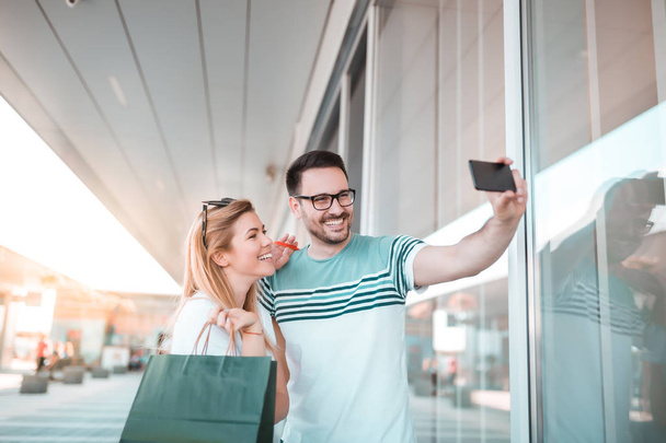 junger Mann mit Brille macht Selfie von sich und seiner Freundin nach dem Einkaufen - Foto, Bild