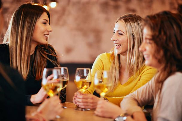 Θηλυκό φίλους πίνοντας κρασί και κουβεντιάζοντας, ενώ κάθεται στο μπαρ. - Φωτογραφία, εικόνα