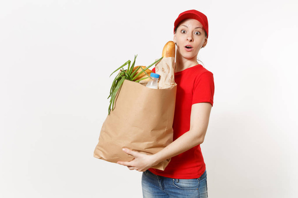 Delivery woman in red uniform isolated on white background. Female courier in cap, t-shirt, jeans holding paper packet with food. Products delivery from shop or restaurant to your home. Copy space. - Photo, Image