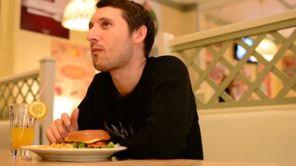 Een man heeft een hamburger in een restaurant en limonade drinken - Video