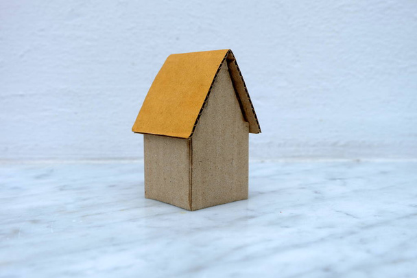 Cardboard House on Marble Floor with White Concrete Wall Background. - Photo, Image