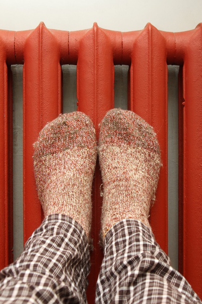 Pies con calcetines de lana calentándose en el radiador
 - Foto, Imagen