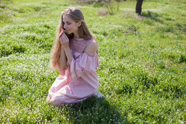 szőke lány rózsaszín ruha gyűjti a virágokat a kertben - Fotó, kép