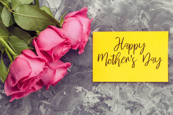ピンクのバラと、灰色のコンクリート背景に幸せな母の日の碑文でイエロー カード - 写真・画像