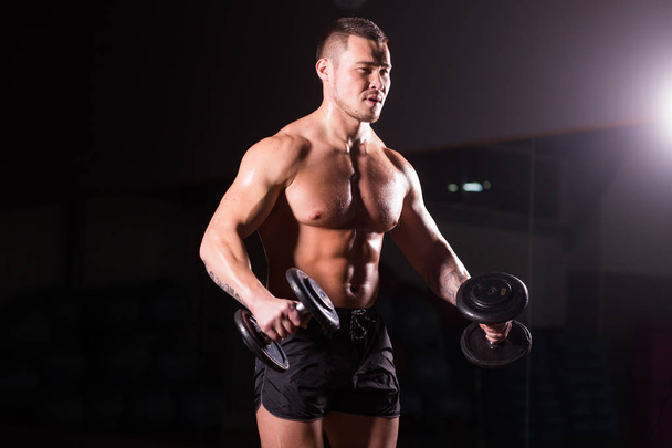 Sporty man doing exercise with dumbbells. Muscular guy on black background. Strength and motivation. - Photo, Image