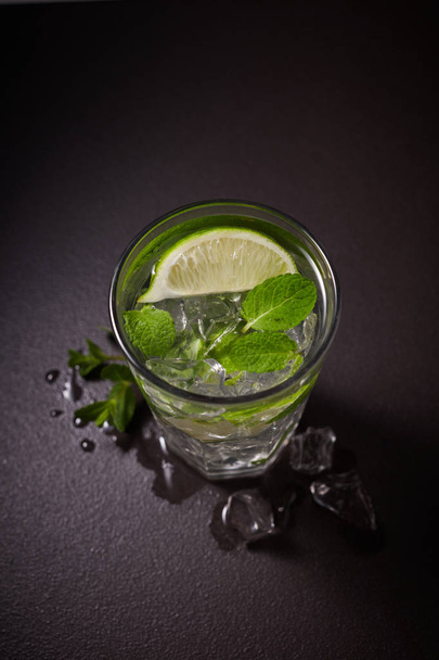 Glass of iced Mojito cocktail and ingredients,  lime, ice and mint leaves on black background, cold summer drink  - Foto, immagini