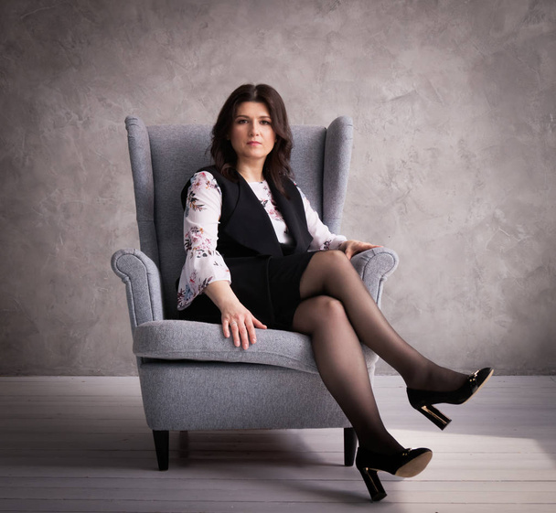 Business lady: a female boss in a gray armchair against a gray wall background. - Φωτογραφία, εικόνα