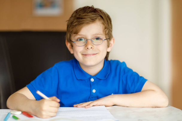 Милый маленький мальчик в очках дома, делает домашнее задание, пишет письма красочными ручками
. - Фото, изображение