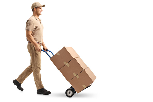 Full length profile shot of a delivery guy pushing a hand truck with boxes isolated on white background - Foto, imagen